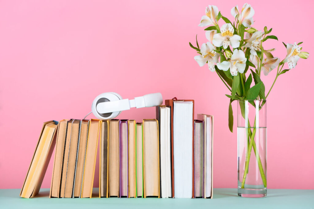 White headphones sitting on top of books on a shelf with flowers on the right