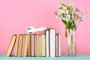 White headphones sitting on top of books on a shelf with flowers on the right