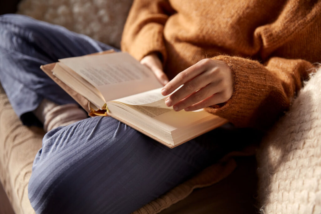 Cropped view of a woman in a mustard-colored sweater reading a book