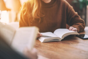Woman reading a book on a table with blurred view of someone else reading in the foreground