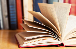 Open book laying on a table with books in the background