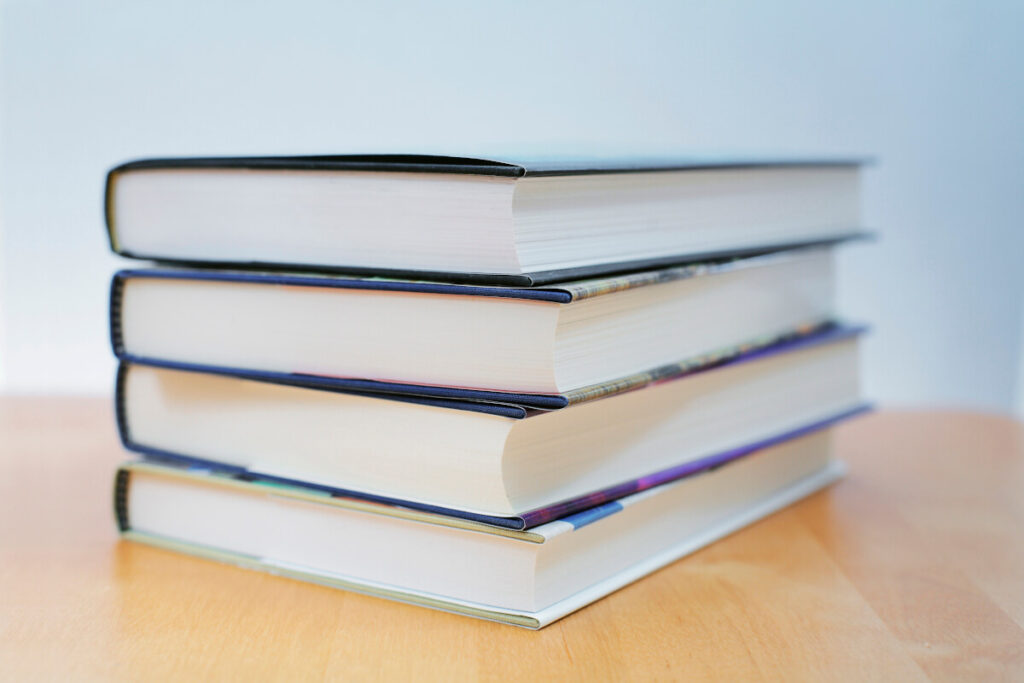 Four new hardcover books stacked on top of each other with pages facing toward the camera