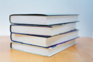 Four new hardcover books stacked on top of each other with pages facing toward the camera